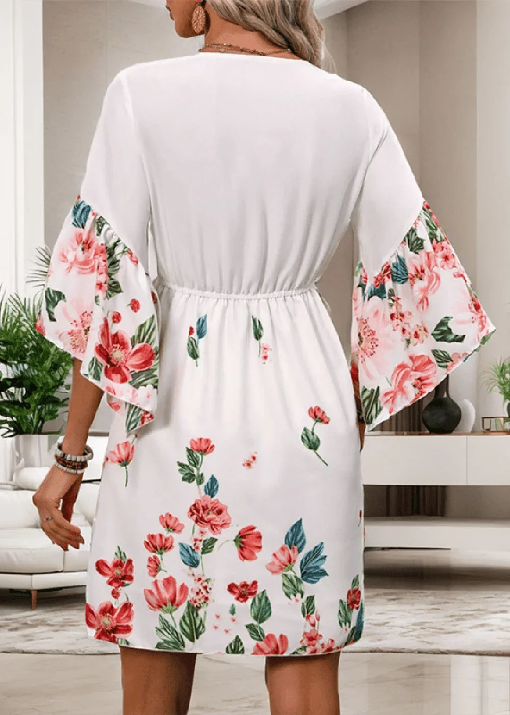 White dress with vibrant floral print on bell sleeves and hem, cinched waist, on model.