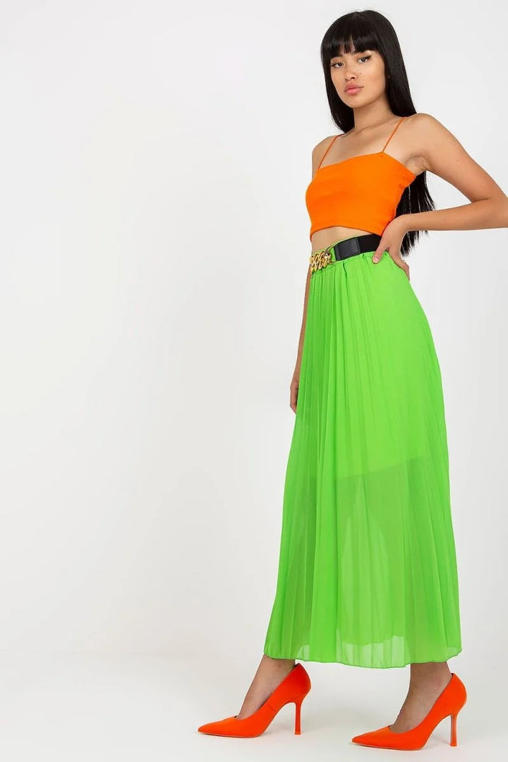 Bright green pleated maxi skirt with a black and gold chain belt, paired with orange heels.