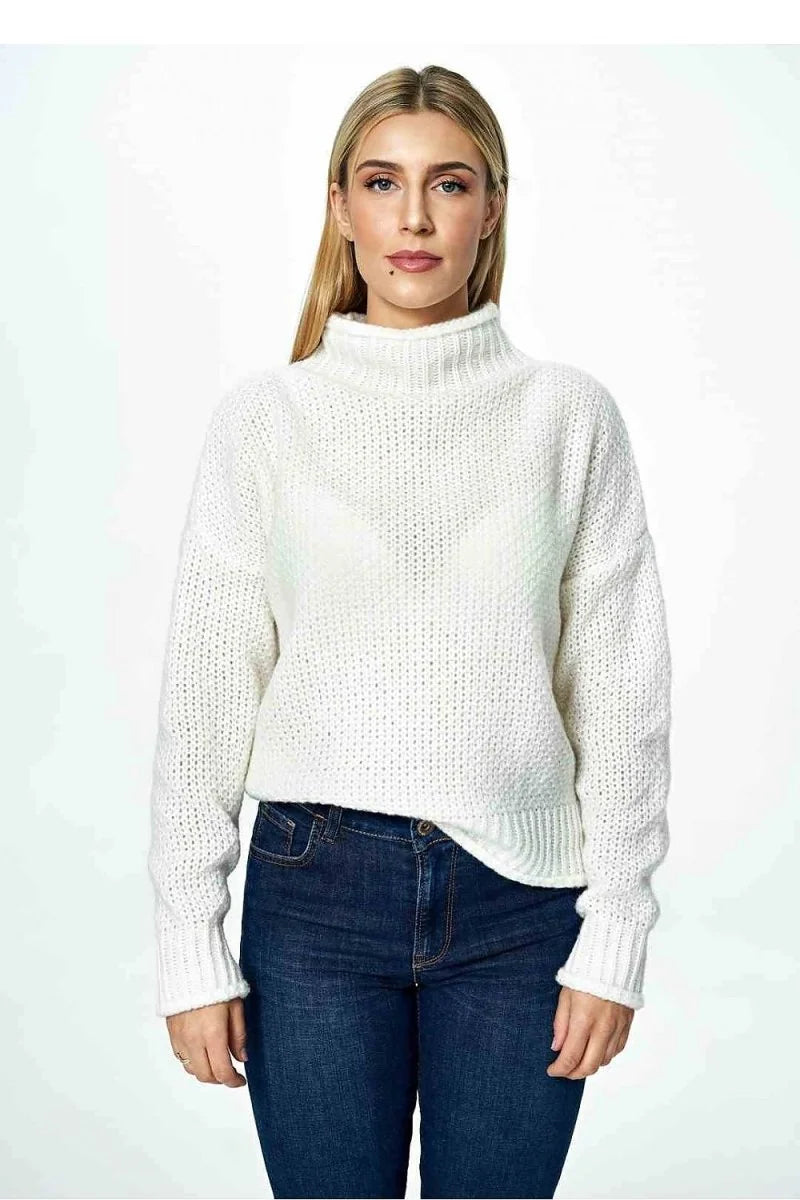 Woman in a textured, cream-colored, high-neck sweater and dark wash jeans.