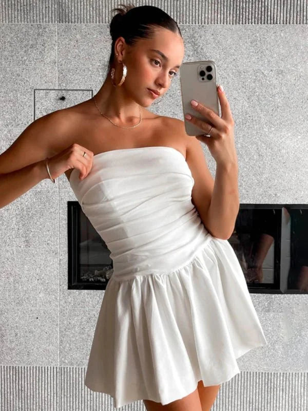 Strapless white ruched bodice mini dress with a full, pleated skirt, shown on a model.