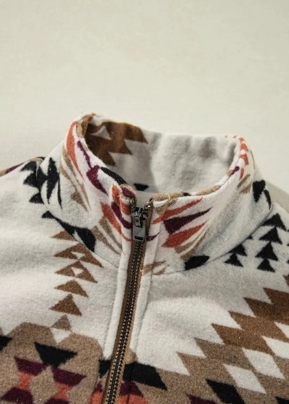 Close-up of a cream jacket with a geometric Southwestern pattern in brown, rust, and black, featuring a zip-up collar.