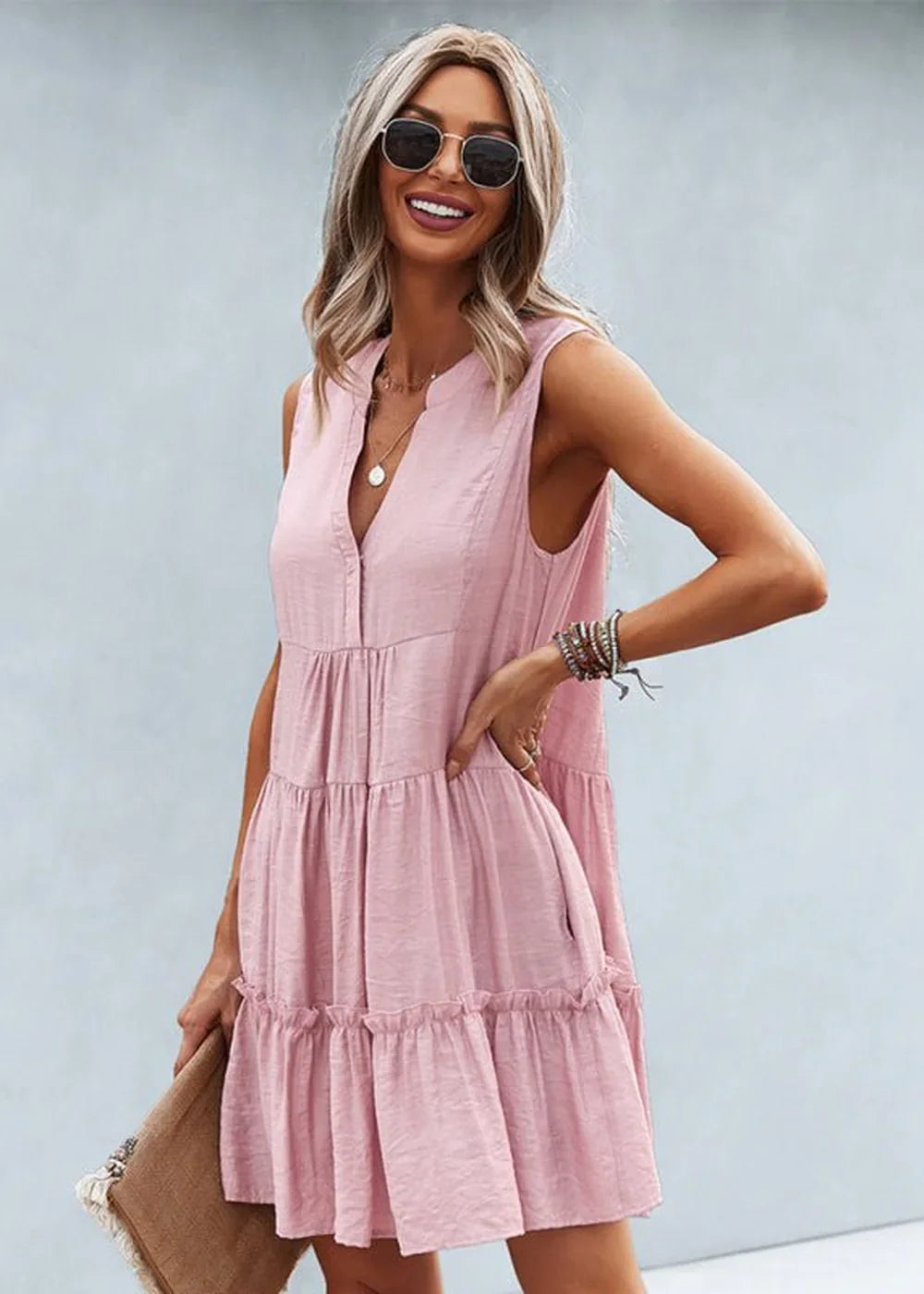 Pink tiered ruffled sleeveless dress with v-neck and a textured fabric on a model.
