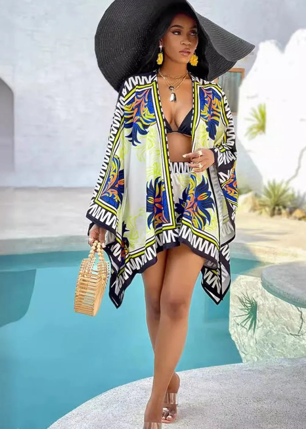 Woman in wide-brimmed hat and vibrant print kimono over bikini, holding a woven bag.