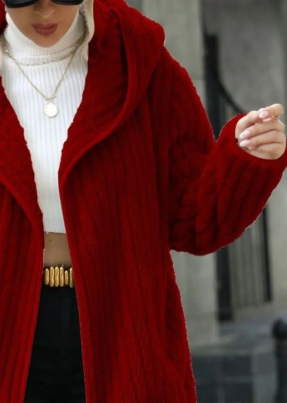 A red, textured knit hooded cardigan with a white turtleneck and layered silver necklaces.
