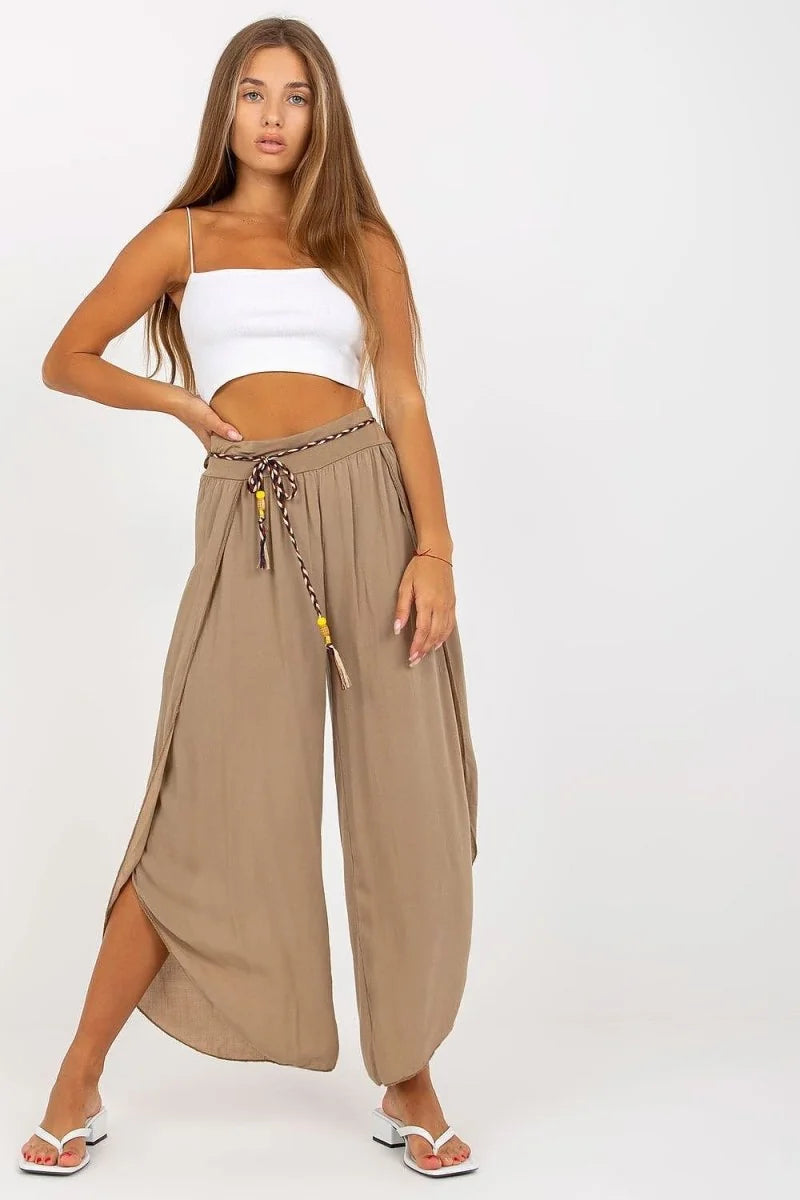 Woman in flowing taupe wide-leg pants with a braided belt and white crop top.