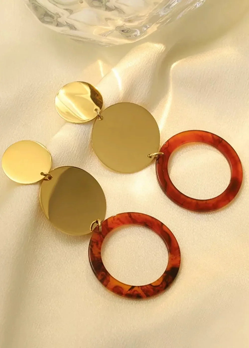 Gold disc earrings with tortoise resin hoops on a silky fabric.