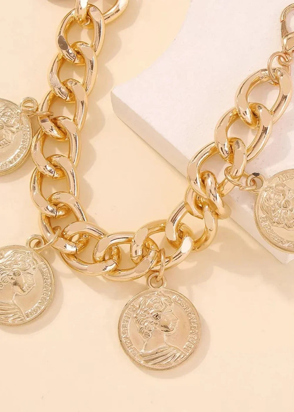 Close-up of a chunky gold chain bracelet with coin charms featuring profiles.