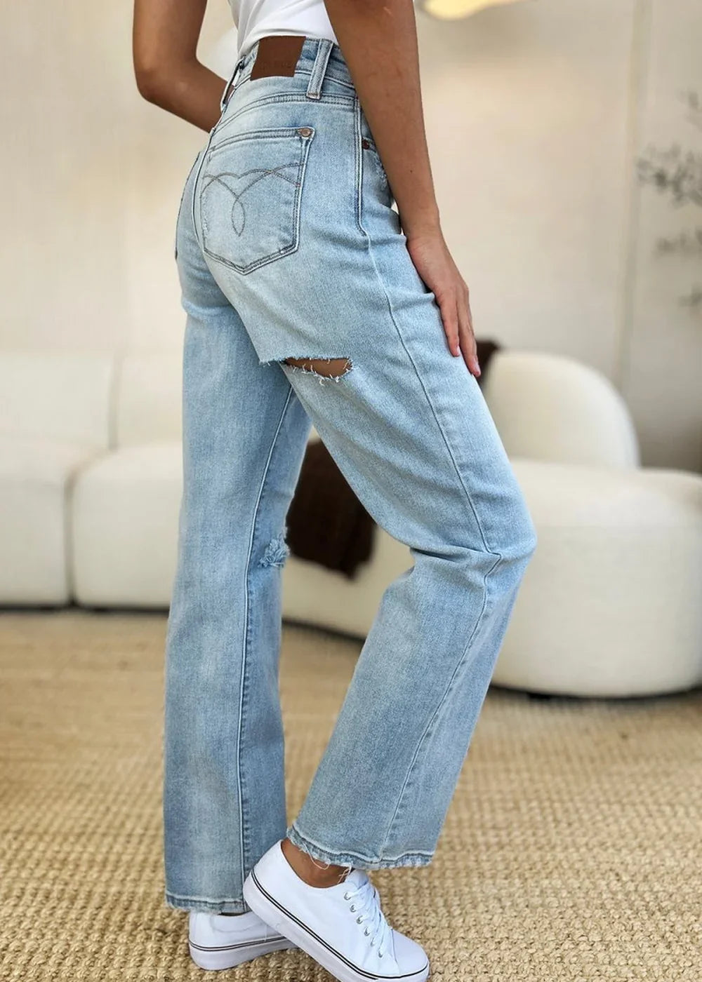 Light wash distressed denim jeans with a ripped accent on the thigh, worn by a model.