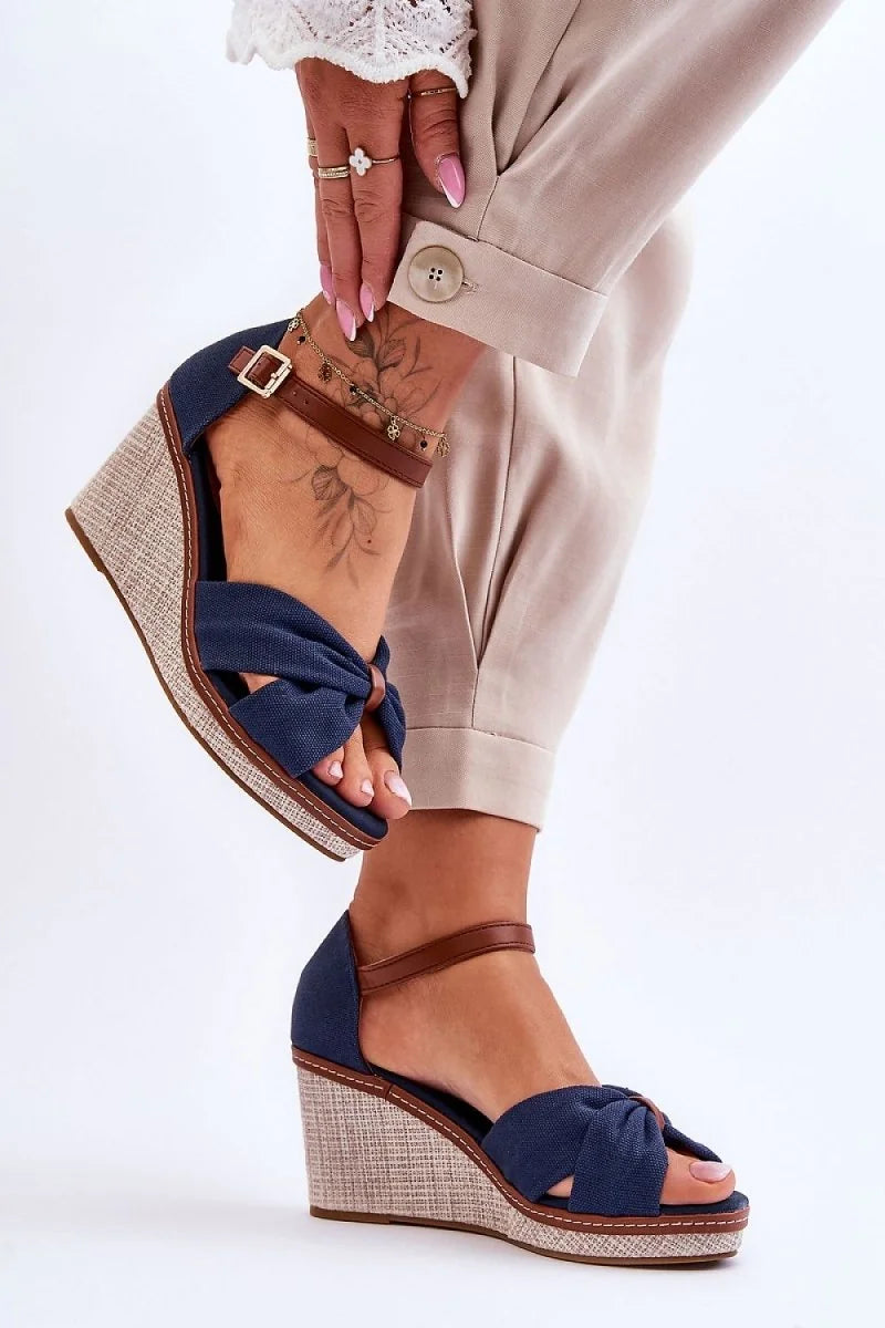 Navy blue canvas wedge sandals with brown ankle strap and knot detail on model.