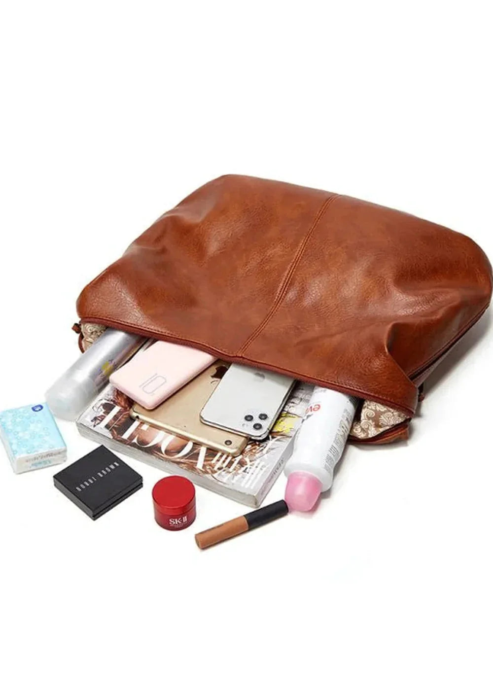 Brown faux leather tote bag spilling out cosmetics, phones, and a magazine.