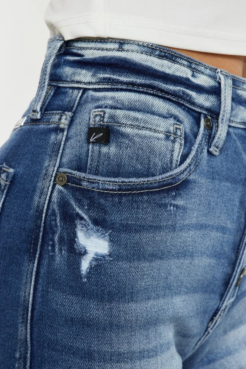 Close-up of distressed medium wash denim jeans with a ripped detail and a black logo tag.