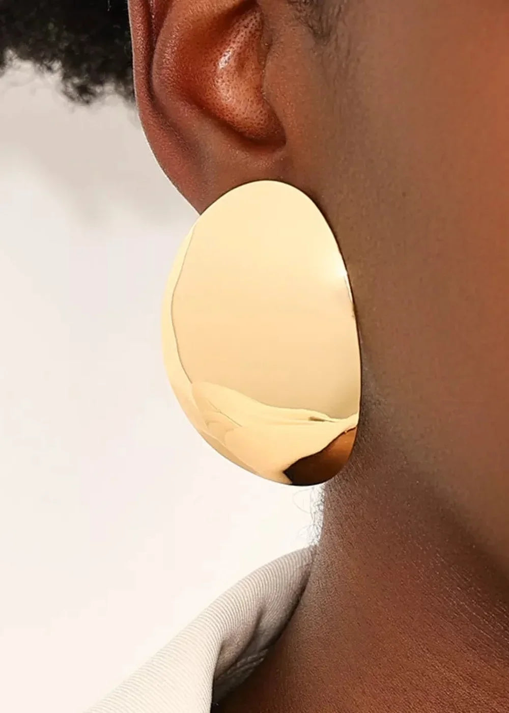 Close-up of a large, shiny, golden oval earring on a dark-skinned ear.