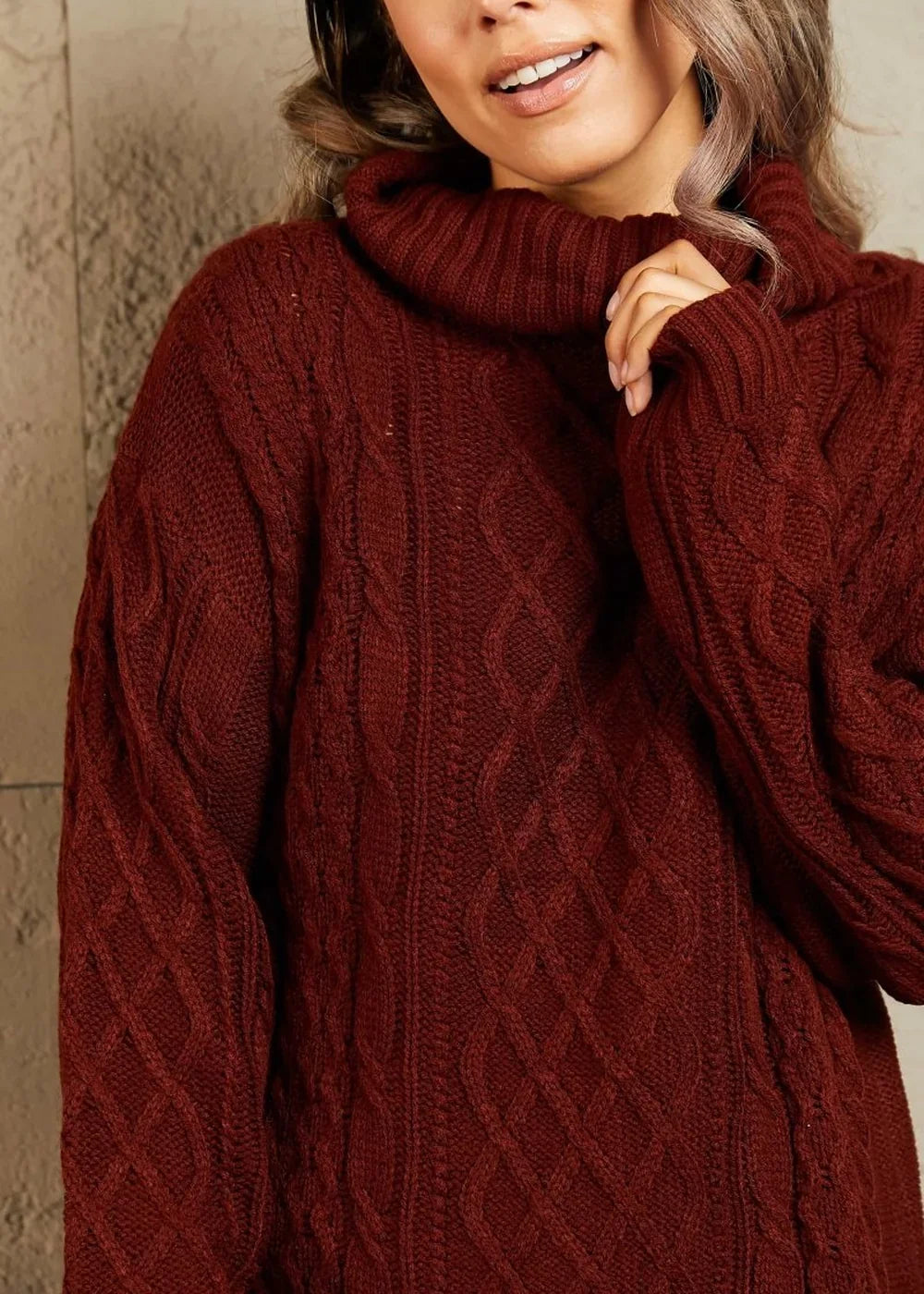 Close-up of a wine-colored cable knit sweater dress with a cowl neck on a model.