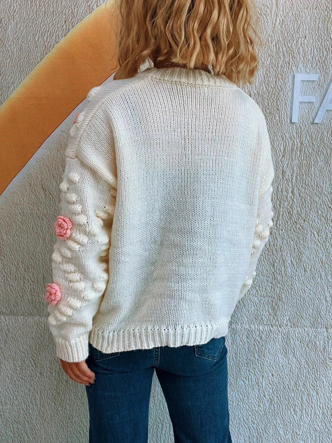 Cream knit sweater with floral applique on sleeves and textured background.