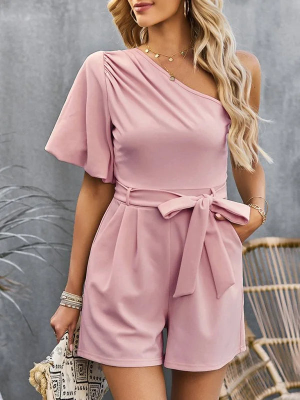 Dusty rose one-shoulder romper with flutter sleeve, belted waist, and pleated shorts.