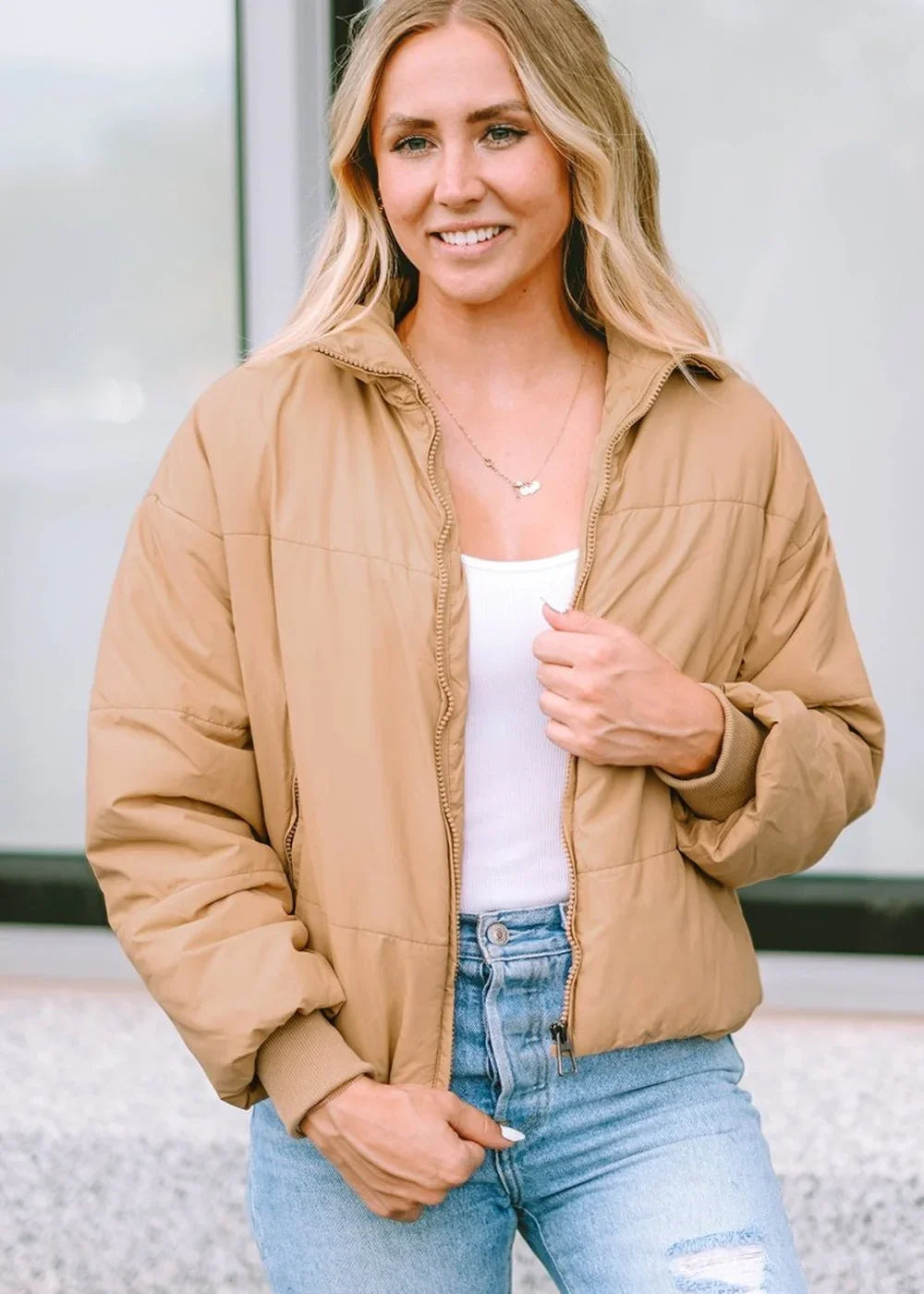 Tan puffer jacket on a woman wearing a white tank top and light wash jeans.