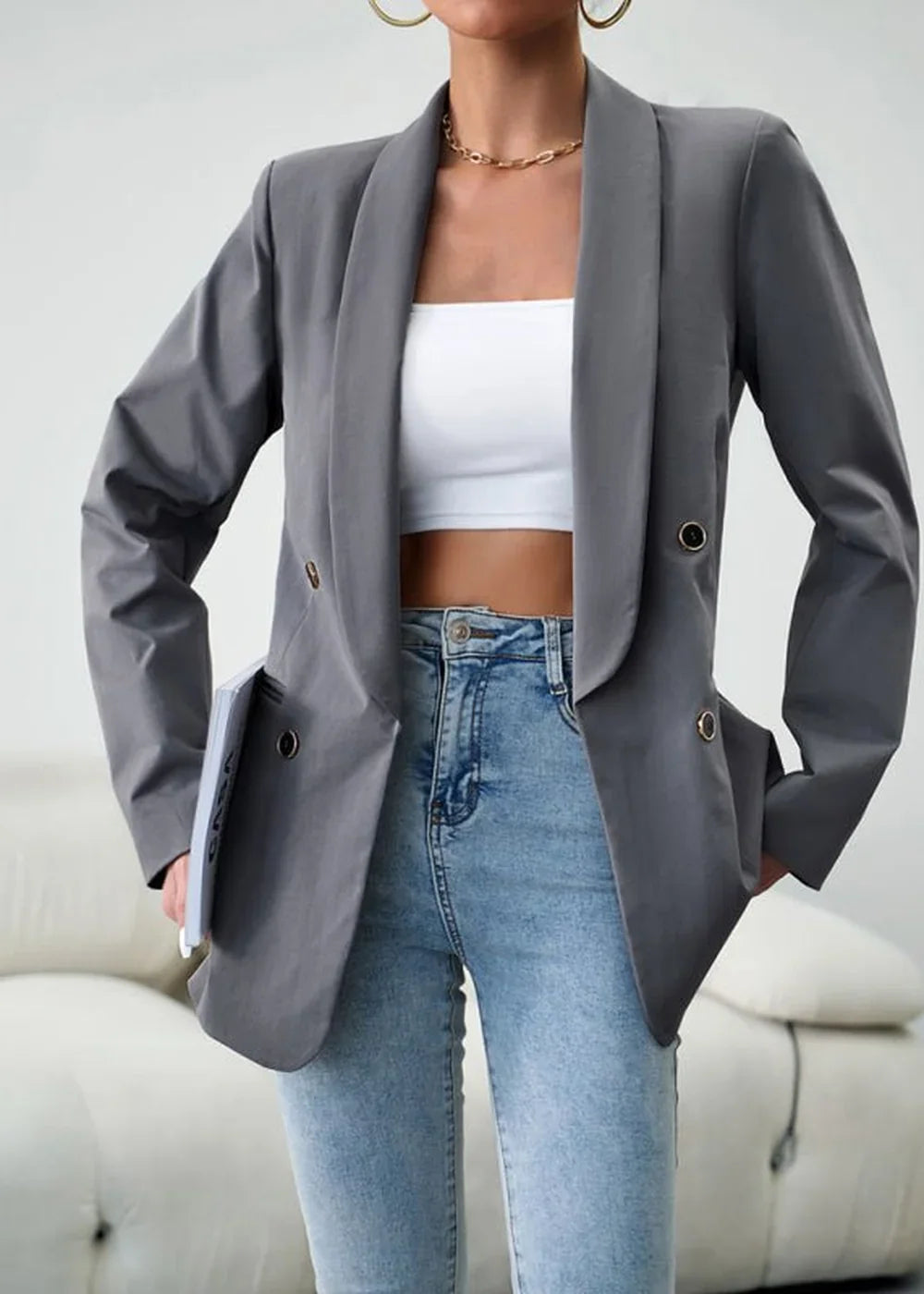 Model wearing a grey blazer with a white crop top and light wash jeans, holding a book.