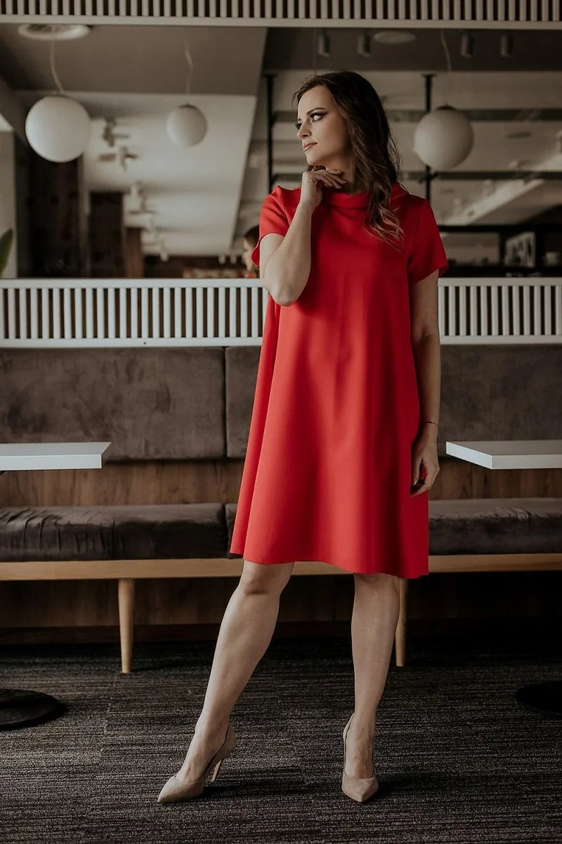 A woman in a red A-line dress with short sleeves and nude heels poses in a restaurant.