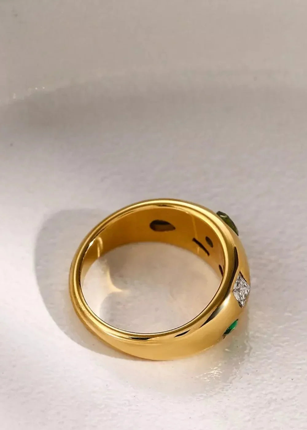 Gold ring with green stones and a diamond accent, showing internal markings.