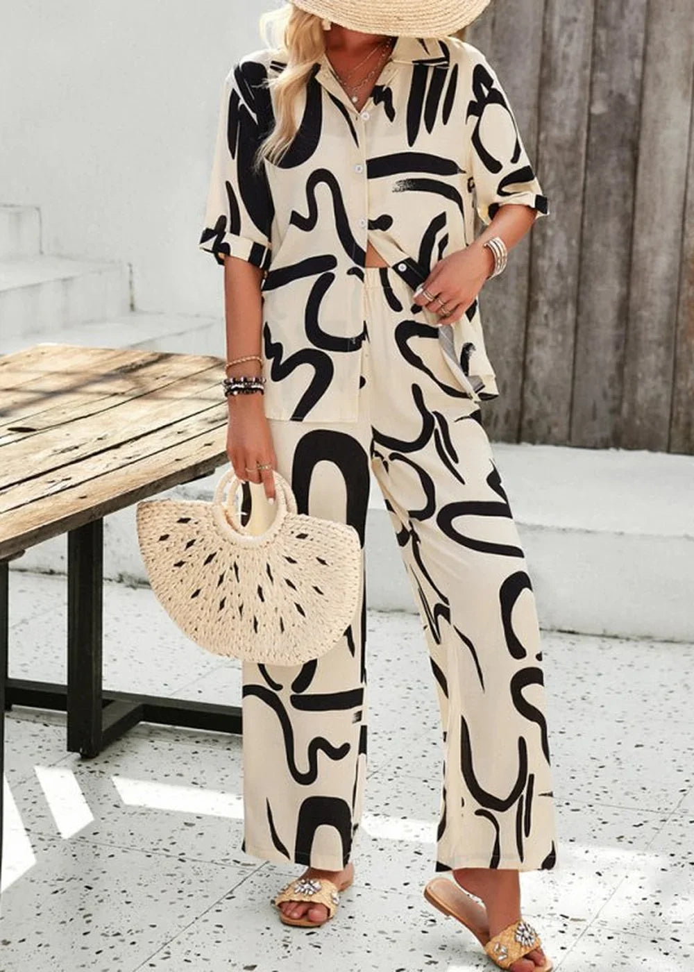 Champlain color pant suit with black abstract print, wide leg pants, and straw bag.