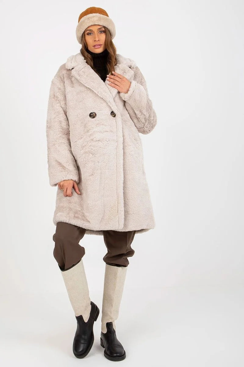Full-length shot of a woman wearing a light beige, fuzzy teddy coat, brown pants, and tall cream boots with black accents.