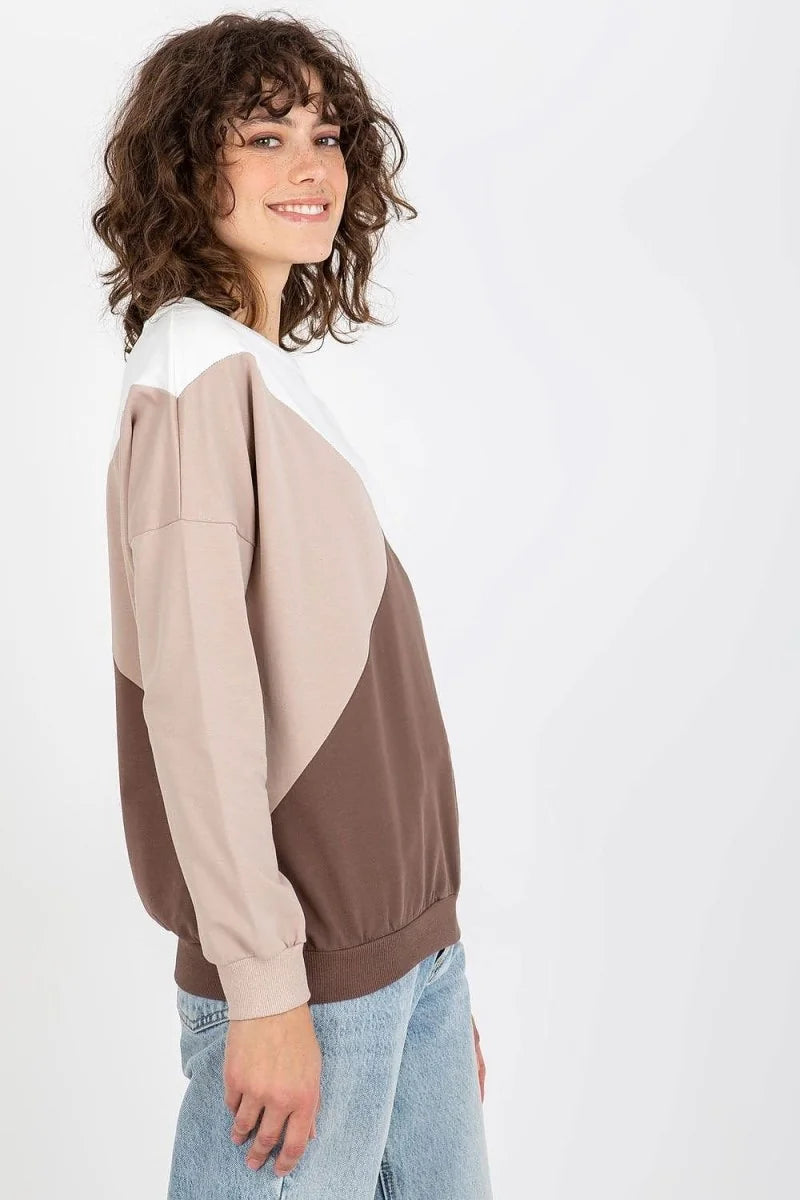 Woman in a colorblock sweatshirt with white, beige, and brown panels, paired with light wash jeans.