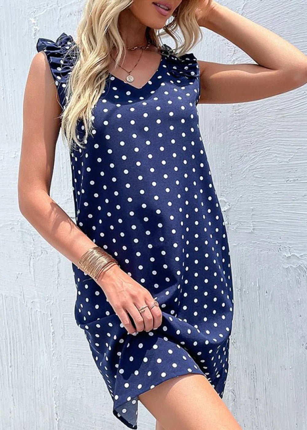 Navy blue polka dot dress with ruffled cap sleeves and gold bangles.