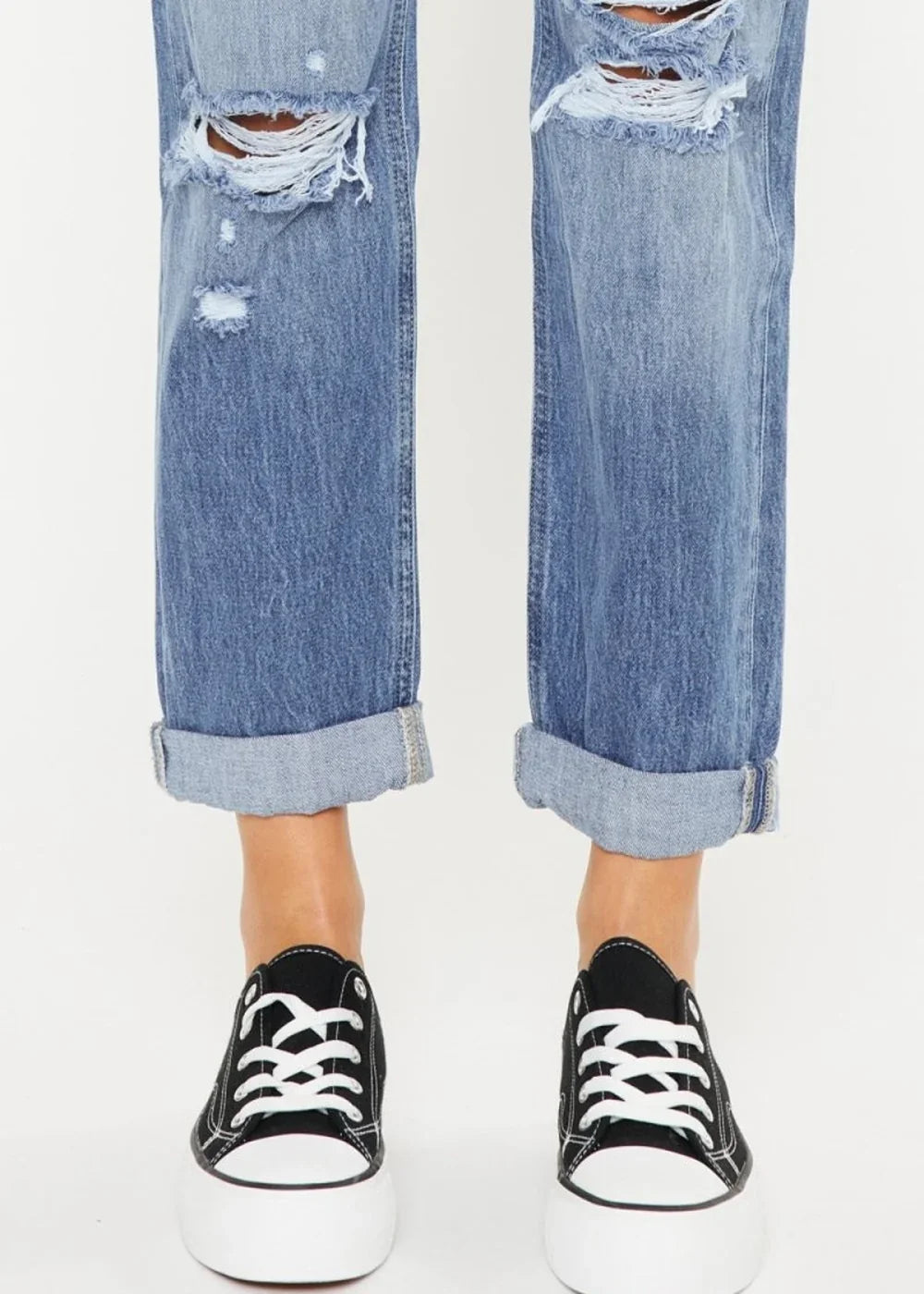 Distressed blue denim jeans with cuffed hems and platform black sneakers.