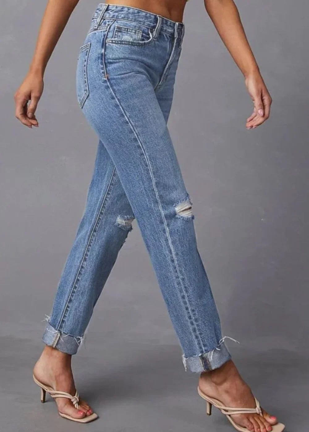 Distressed light wash denim jeans with cuffed hems and ripped knees, worn by a model.