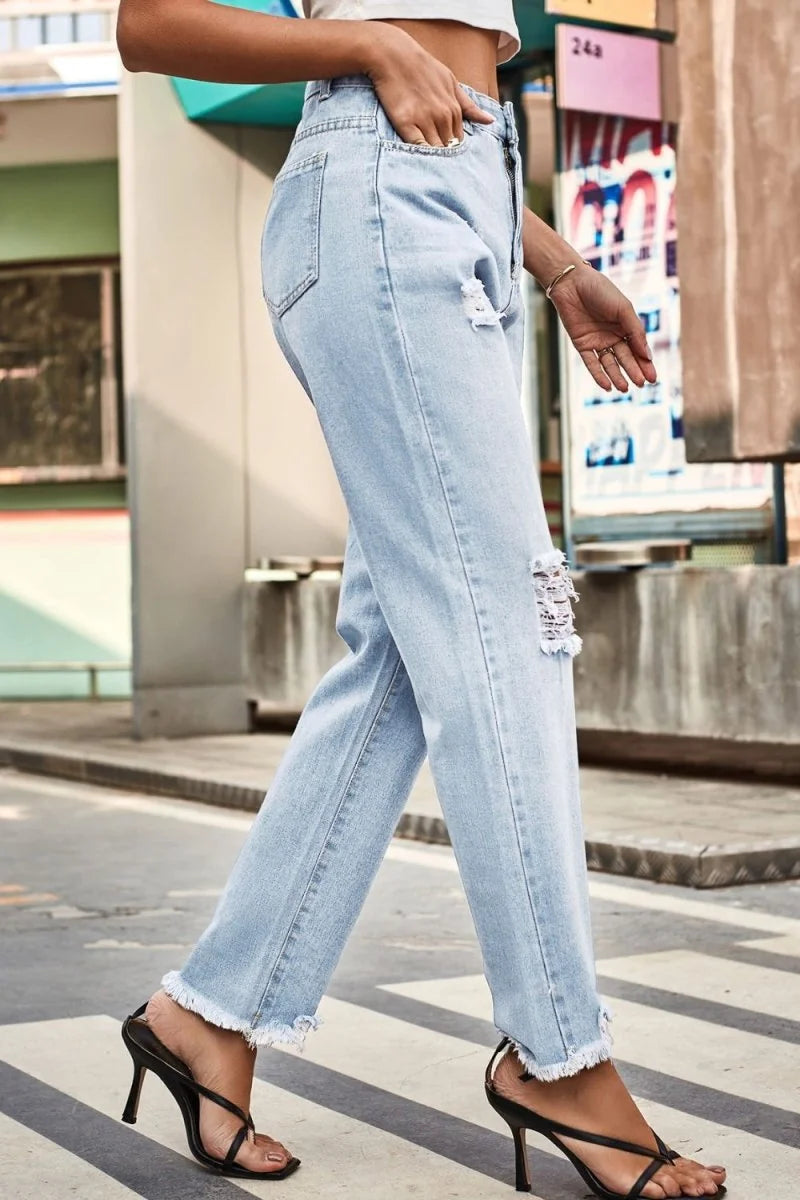 Light wash distressed denim jeans with frayed hems and a loose fit, shown on a model.