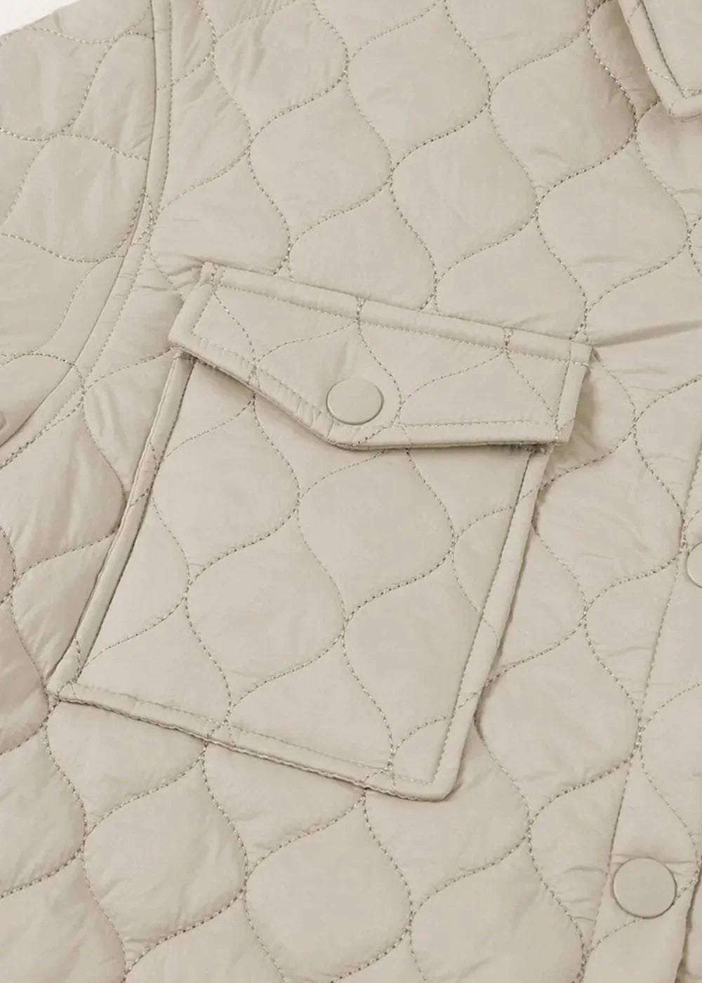 Close-up of a light beige quilted jacket with a diamond pattern and a single pocket with a button closure.