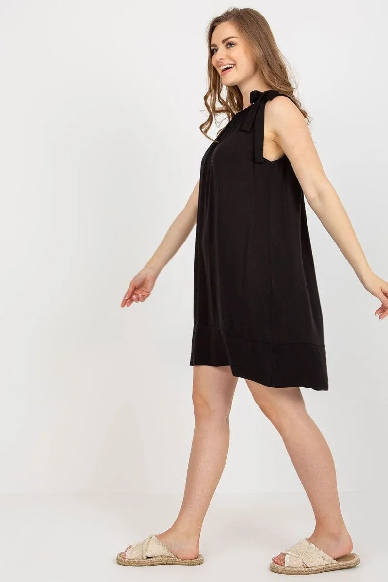 Woman in a loose-fit, sleeveless black viscose mini dress with tie shoulders and espadrille slides.