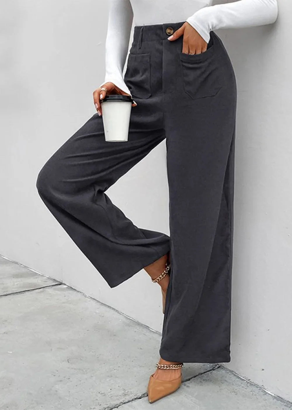 Close-up of dark gray wide-leg pants with pockets and a gold ankle chain on a model.