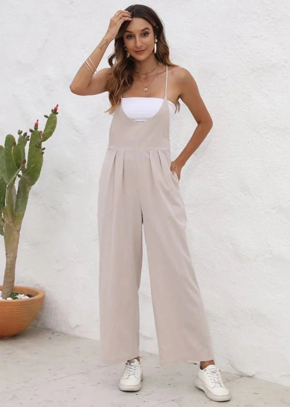 Full-length shot of a woman wearing a beige wide-leg jumpsuit with a white top and white sneakers.