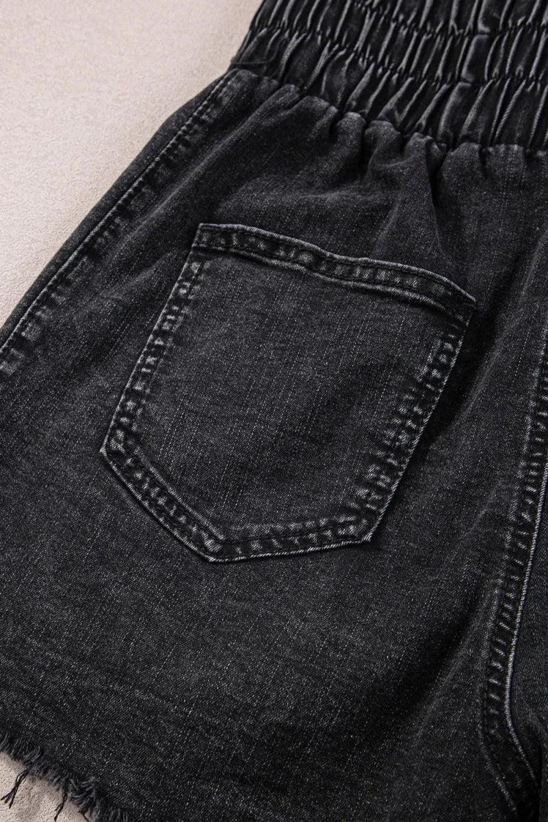 Close-up of distressed black denim shorts with elastic waistband and frayed hem.