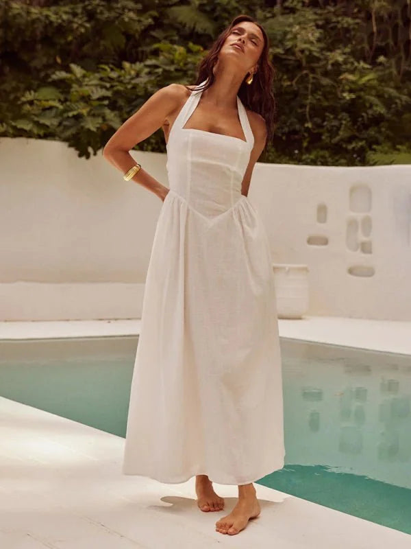 Woman in a white halter maxi dress with a fitted bodice and full skirt, posing by a pool.