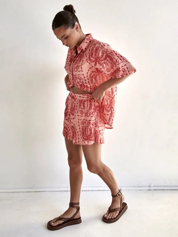 Pink crop top and shorts set with red palm tree print, worn by a model with brown sandals.