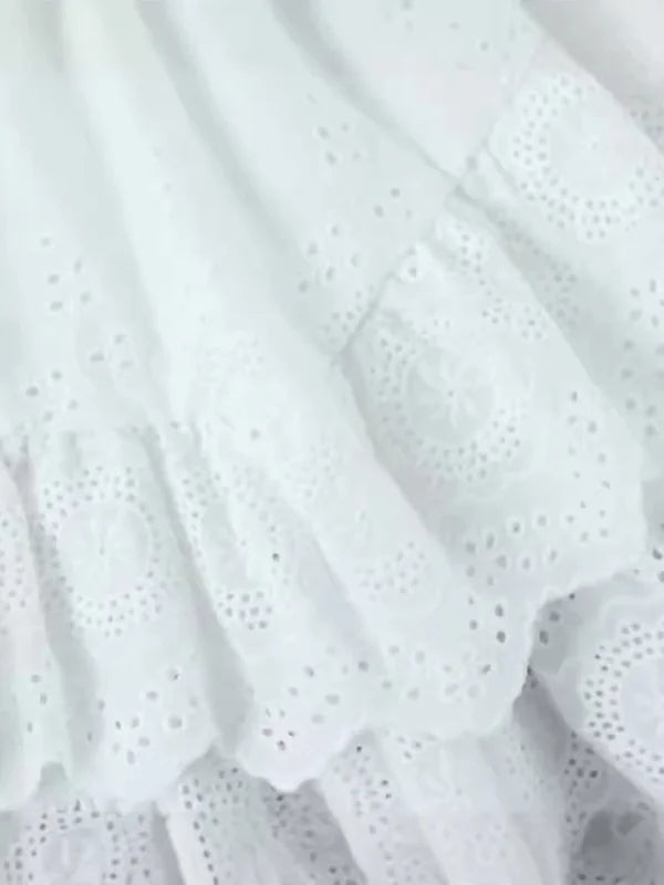 Close-up of white eyelet fabric with ruffled tiers and circular floral embroidery.