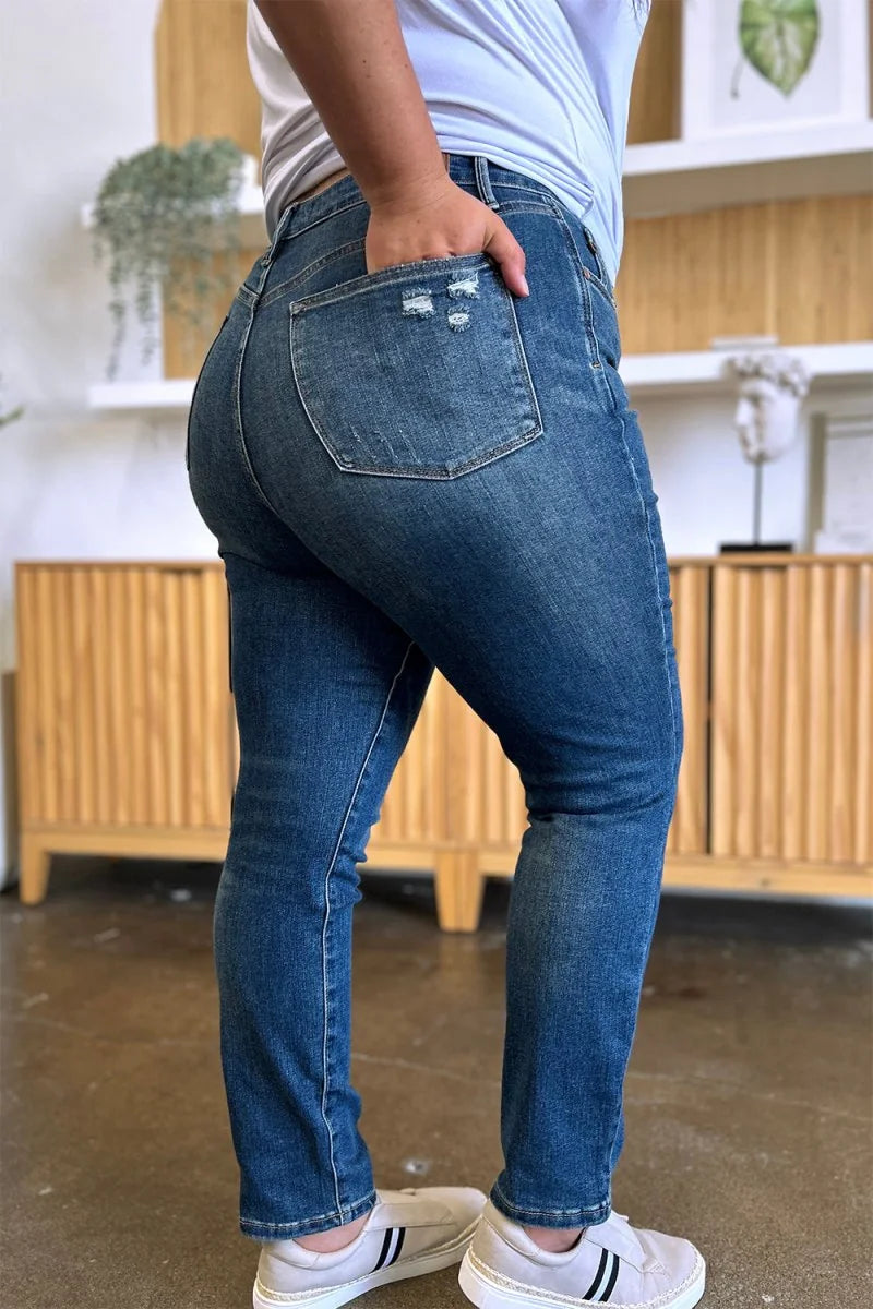 Distressed mid-wash denim jeans with a distressed pocket detail, shown on a model from the side.