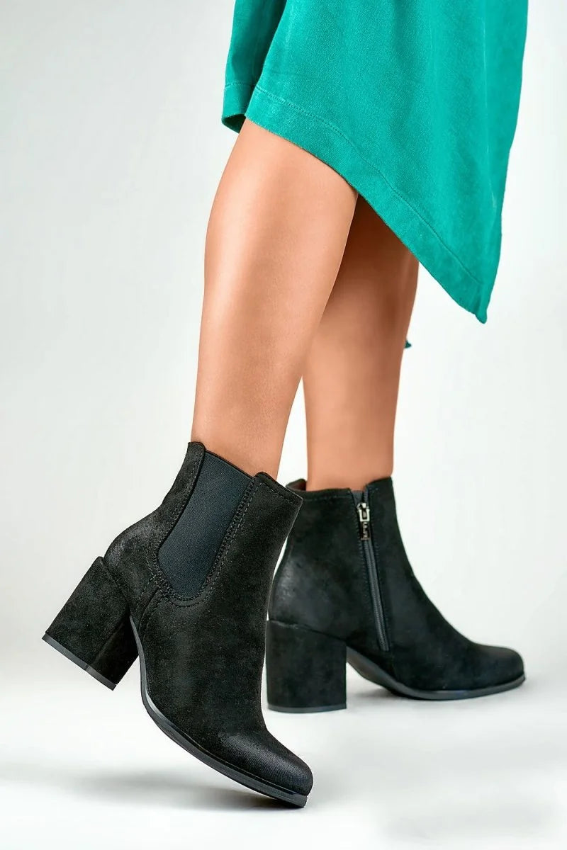 Black suede ankle boots with chunky block heels and side zippers on a model.