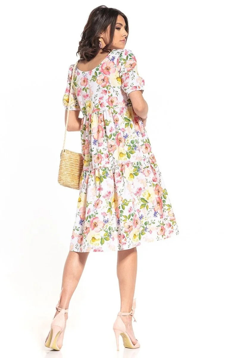 White cotton day dress with a loose floral pattern of pink, yellow, and blue flowers, tiered skirt, and short puff sleeves.