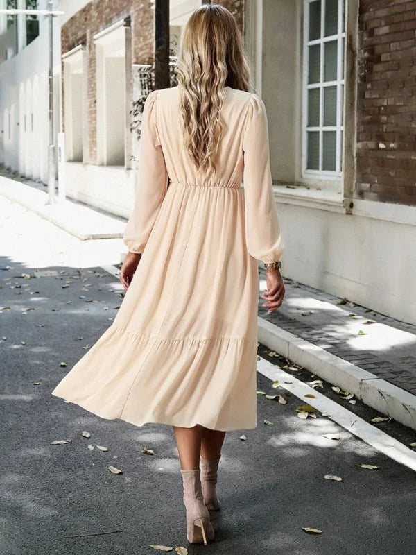 Cream tiered midi dress with long sleeves, cinched waist, and ruffled hem.