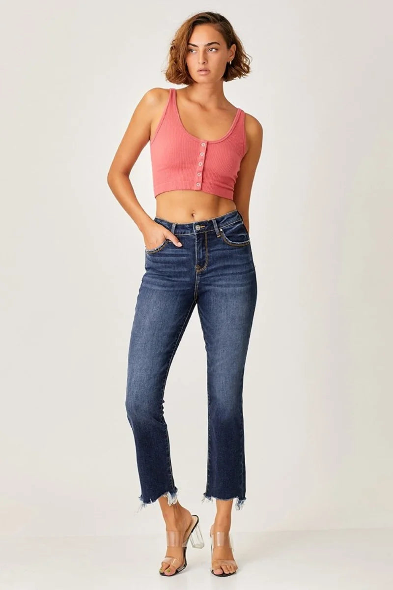 Full-length shot of a woman wearing high-waisted, dark wash denim jeans with a frayed hem and a pink ribbed crop top.