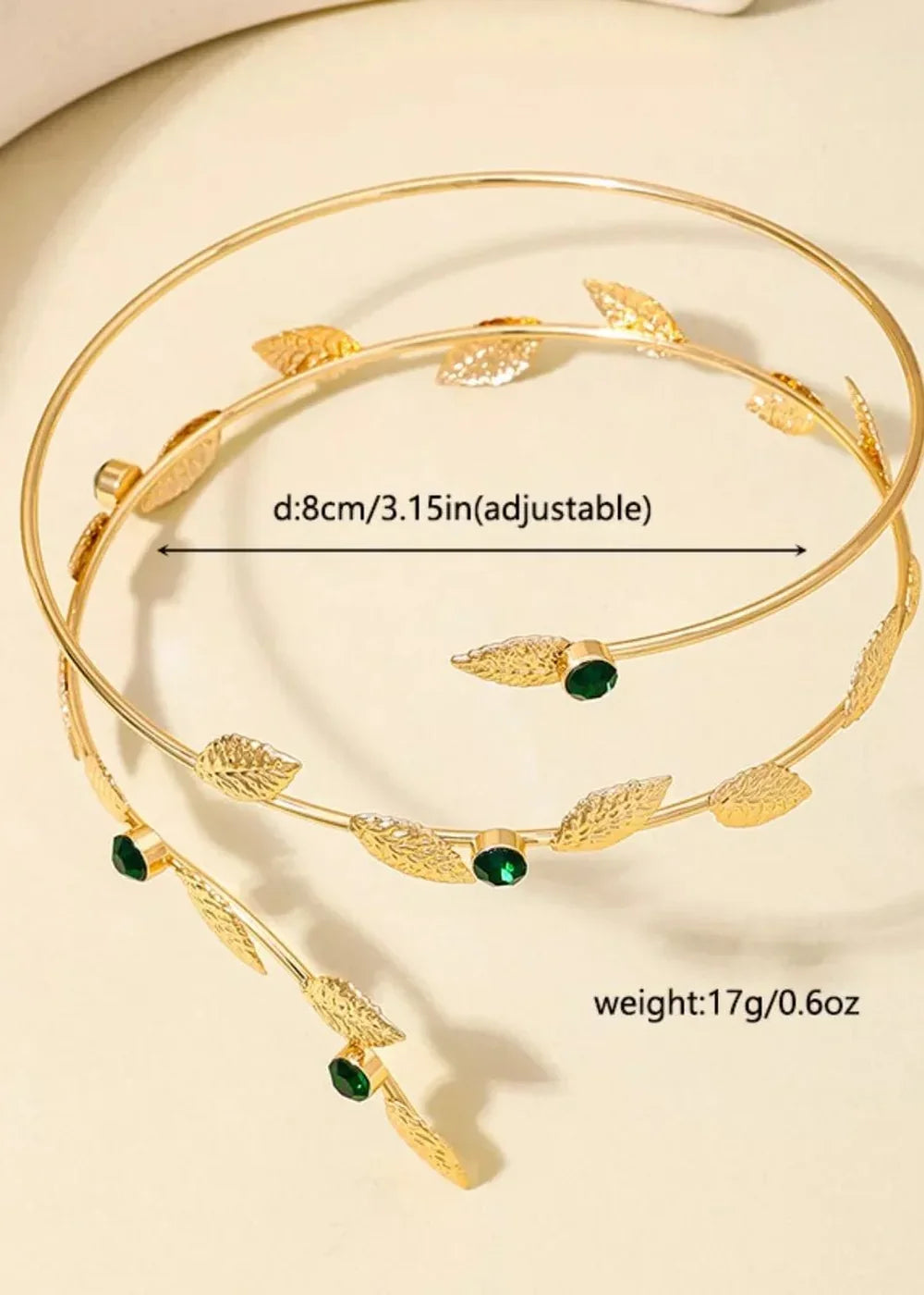 Gold-toned arm cuff with leaf details and green gems, showing adjustable size and weight.