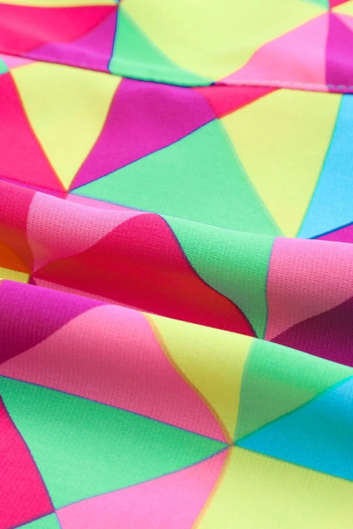 Close-up of multicolor geometric pattern fabric with vibrant pink, yellow, and green triangles and folds.