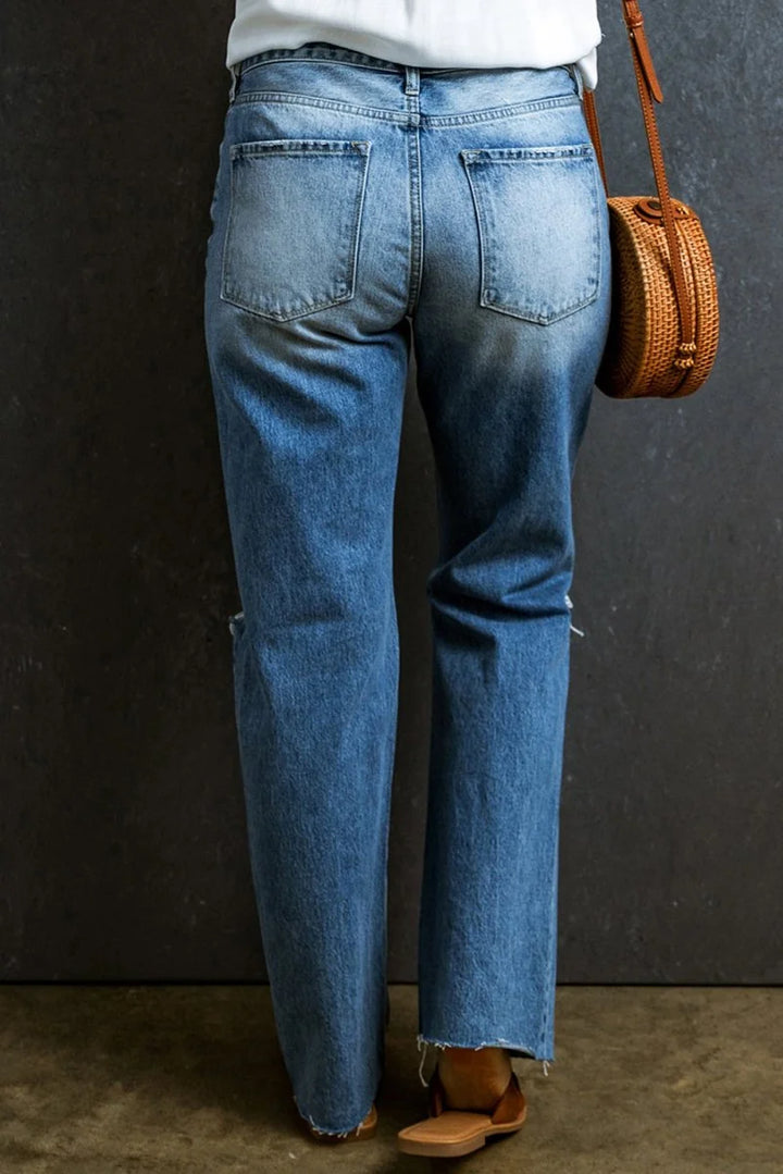 Distressed medium-wash denim jeans with a frayed hem and a subtle rip on the left leg.