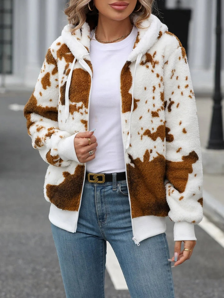 Fuzzy white and brown cow print zip-up hoodie with gold belt and blue jeans on model.