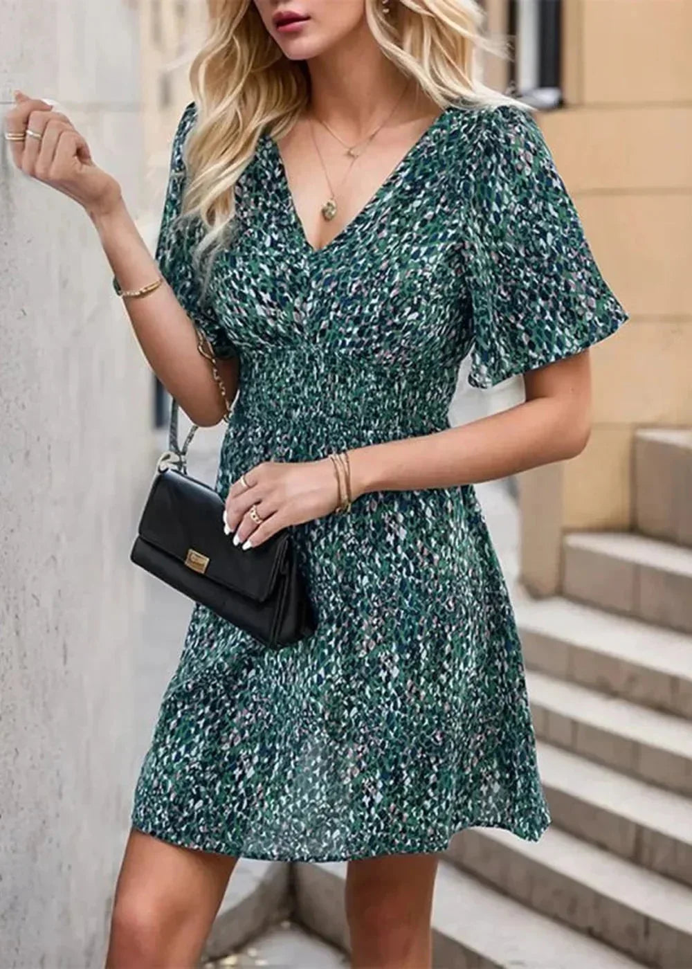 Green patterned v-neck dress with smocked waist and flutter sleeves, held by a model.