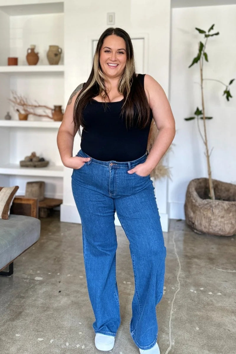 Woman in high-waisted, wide-leg blue jeans and a black tank top, hands in pockets.