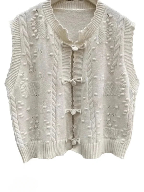 Cream cable knit vest with knot button closure and textured details.